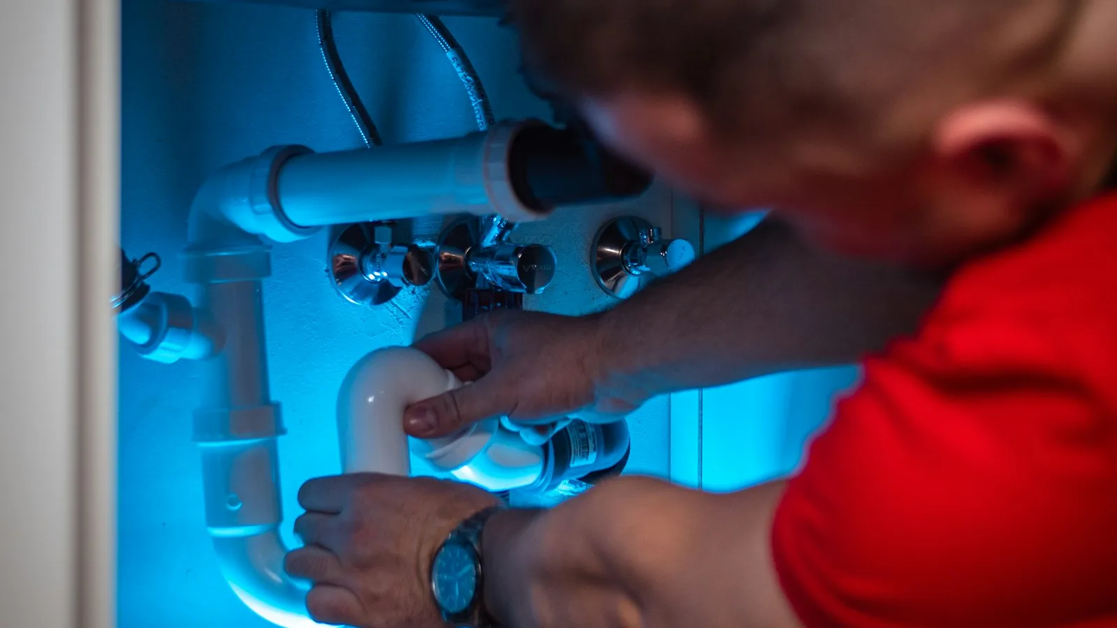 An open kitchen cabinet showing an under-sink water filter system connected to the cold water line